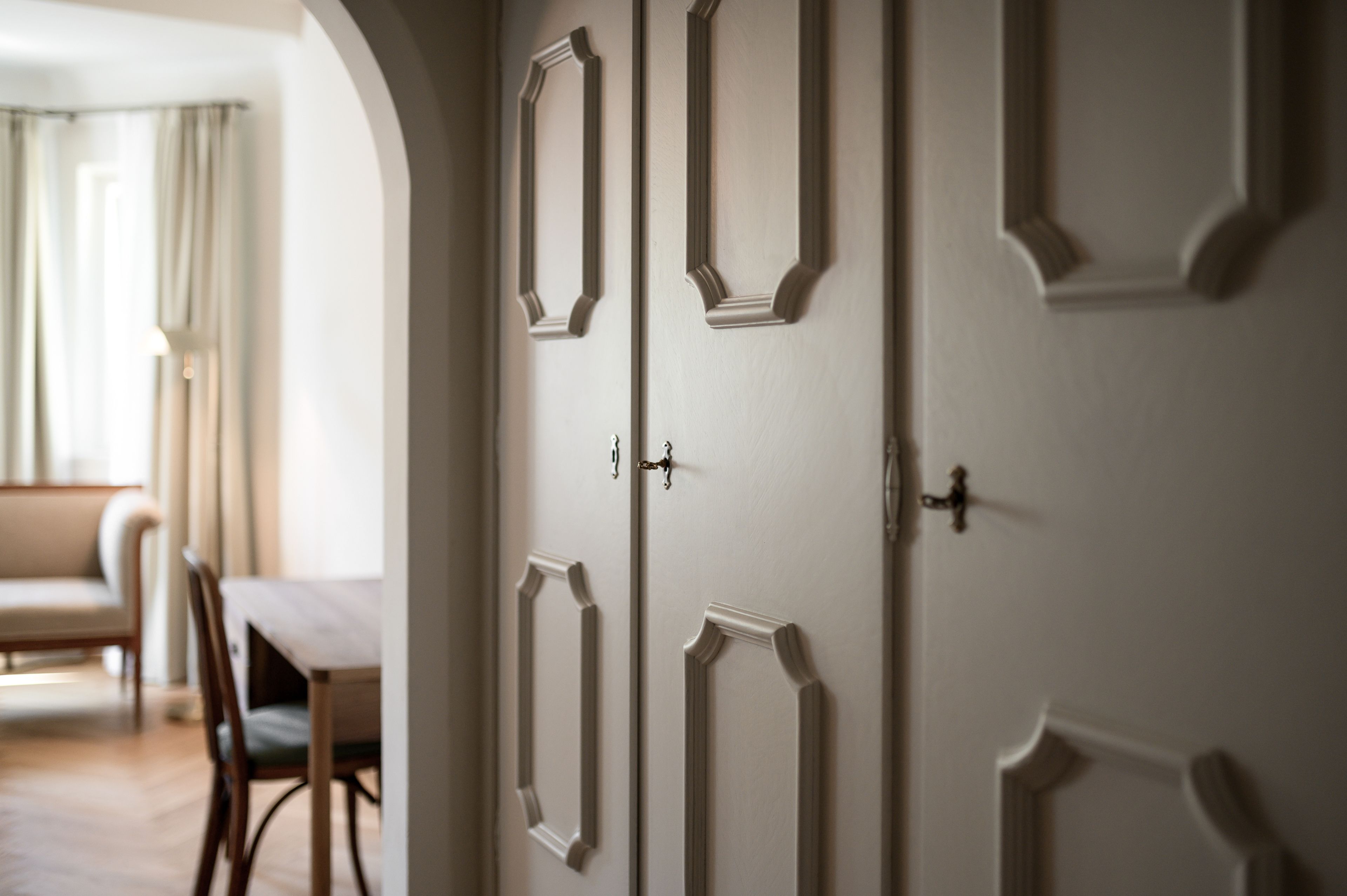 Una habitación con una puerta blanca grande con molduras decorativas, una mesa de comedor con sillas y una ventana con cortinas.