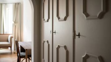 Una habitación con una puerta blanca grande con molduras decorativas, una mesa de comedor con sillas y una ventana con cortinas.