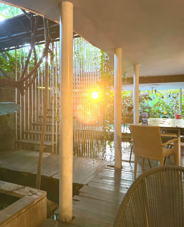 An outdoor seating area with wooden tables and chairs, surrounded by a fence and greenery.