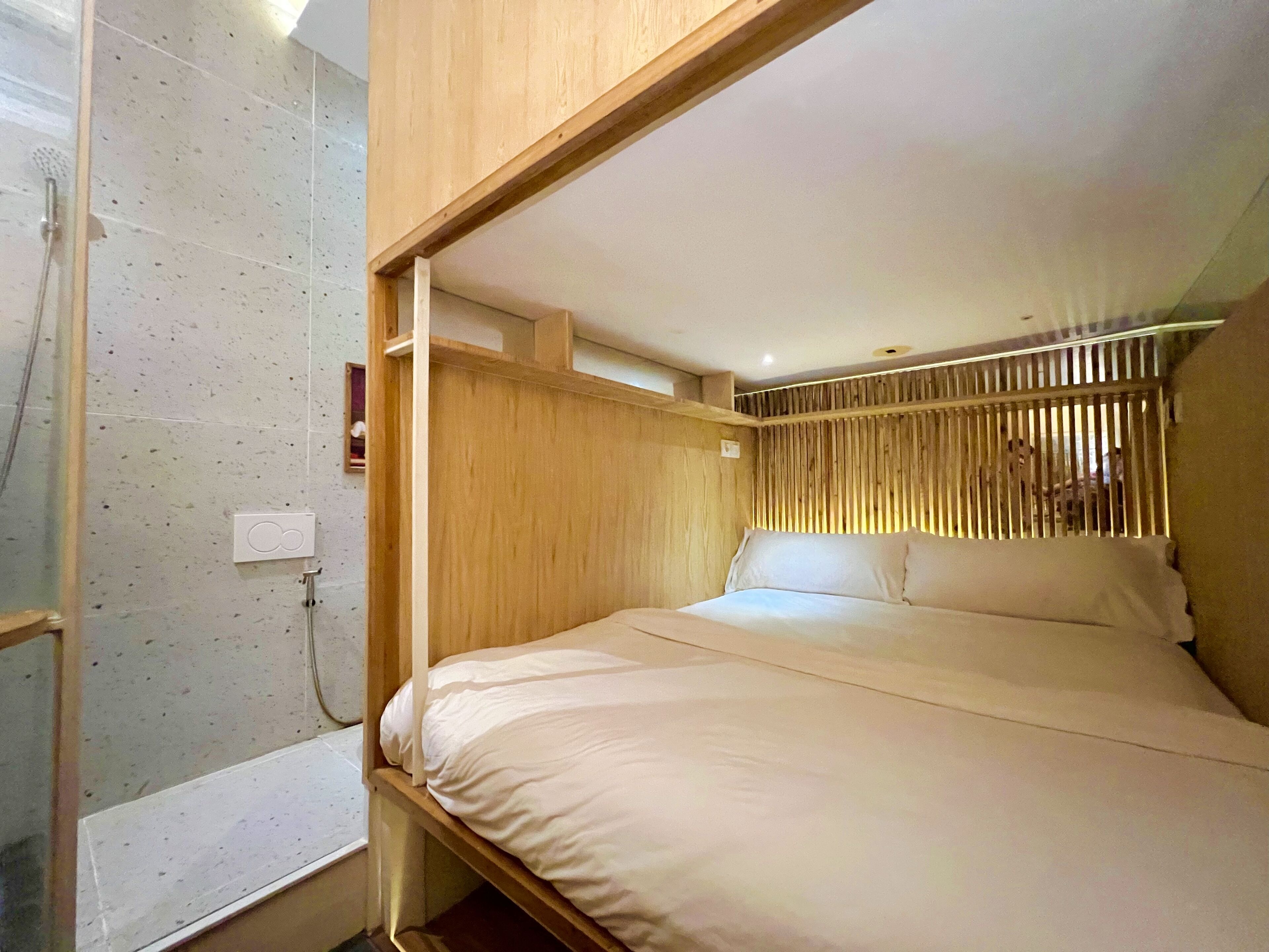 A compact room with a bed, a shower, and a wooden partition.