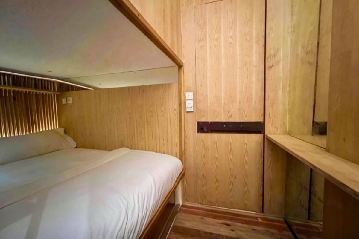 A wooden bunk bed with a headboard, a wooden wardrobe, and a small shelf.