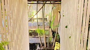 A wooden pergola structure with vertical slats, leading to a garden area with plants and a caution sign. - The Hide Hostel at Canggu - Adults Only (Canggu)