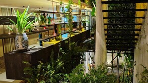 A modern interior with a wooden staircase, a bar area with shelves, and various plants. - The Hide Hostel at Canggu - Adults Only (Canggu)
