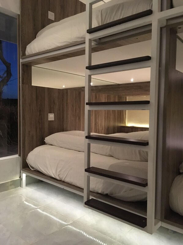 A multi-level bunk bed with white bedding, wooden paneling on the walls, and a modern design. - The Hide Hostel at Canggu - Adults Only (Canggu)