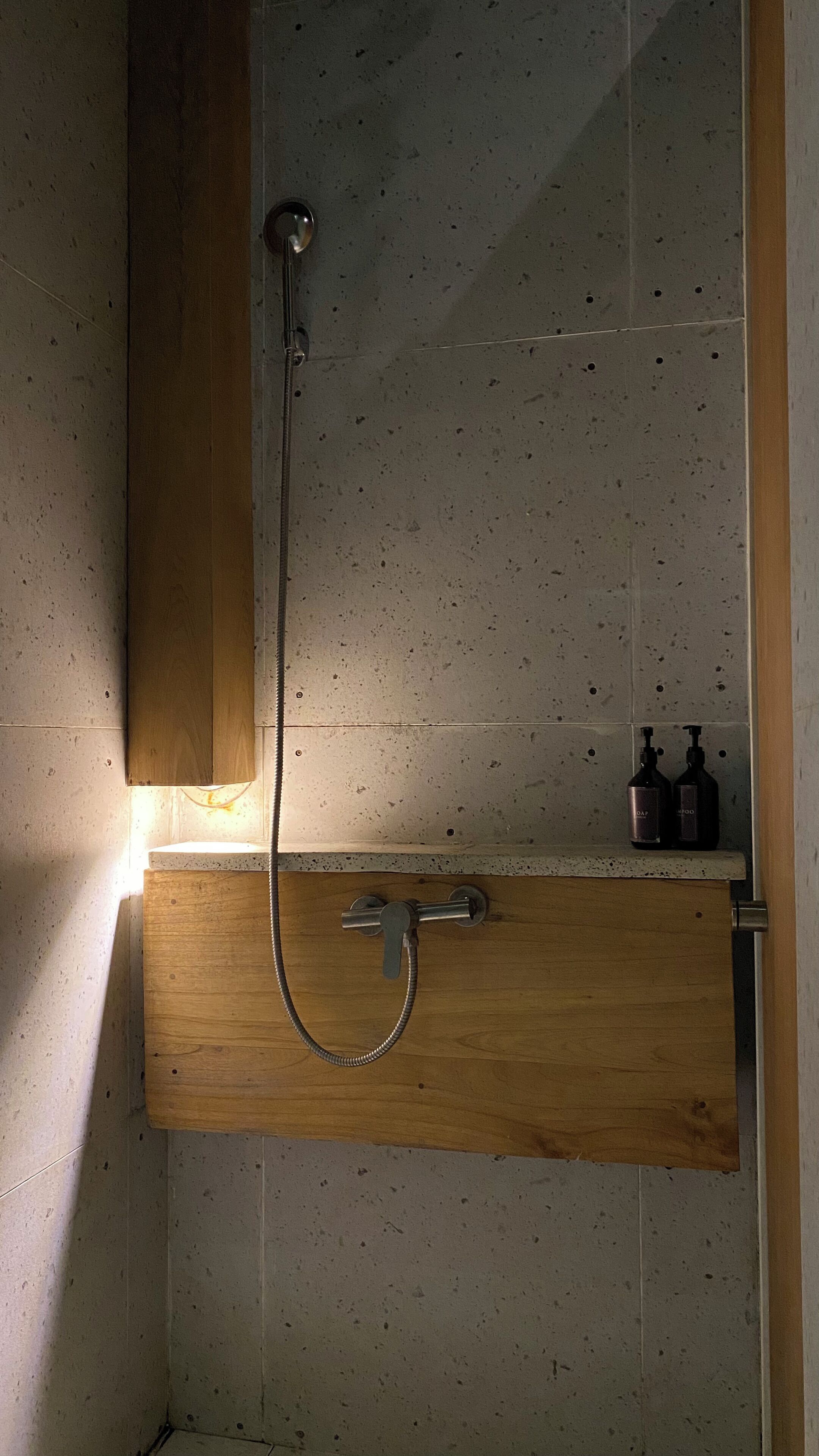 Een douche met een houten kast eronder, een metalen douchekop en twee flessen op een plank.