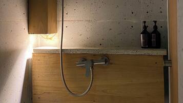 Een douche met een houten kast eronder, een metalen douchekop en twee flessen op een plank.