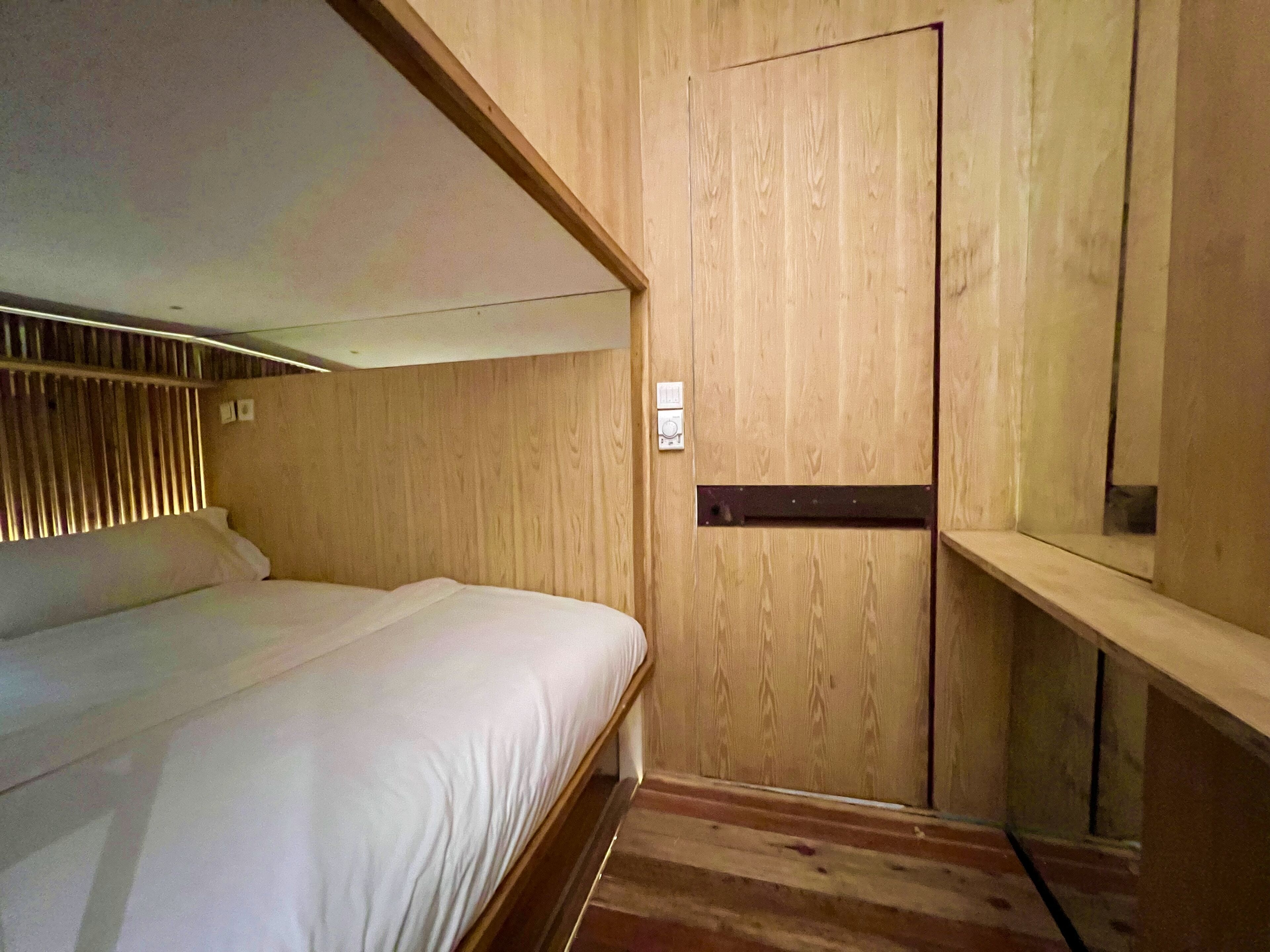 Una habitación pequeña con una cama, paredes de madera, una puerta y un estante.