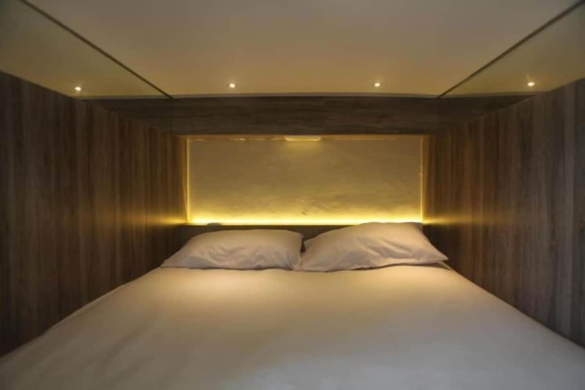A modern bedroom with a wooden panel wall, a large bed with white bedding, and recessed lighting.
