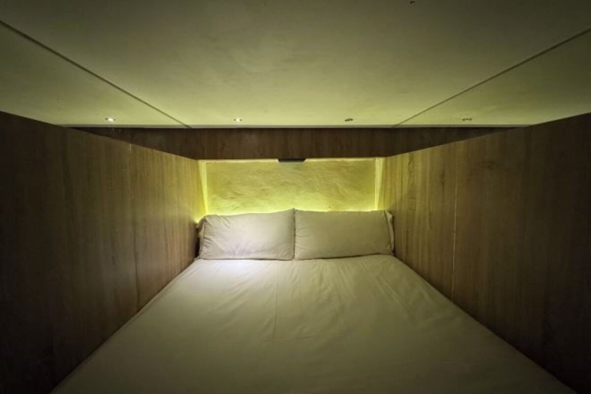A room with a bed centered against a wall, with a sloped ceiling and recessed lighting.