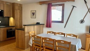 A kitchen with wooden cabinets, a dining table with chairs, a small refrigerator, and a window with a curtain. - 4-Room Rental with Balconies for 8 in Puy-Saint-Vincent (Puy-Saint-Vincent)