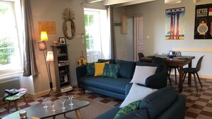 A living room with a blue sofa, a coffee table, and a dining area with a table set for two. - GITE DE CHARME 3 Etoiles, Label Clef Verte, Wifi Fibre, Futuroscope 86800 LAVOUX (Lavoux)