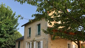 A two-story stone building with white shutters, a small balcony, and a garden area with potted plants and outdoor furniture. - GITE DE CHARME 3 Etoiles, Label Clef Verte, Wifi Fibre, Futuroscope 86800 LAVOUX (Lavoux)