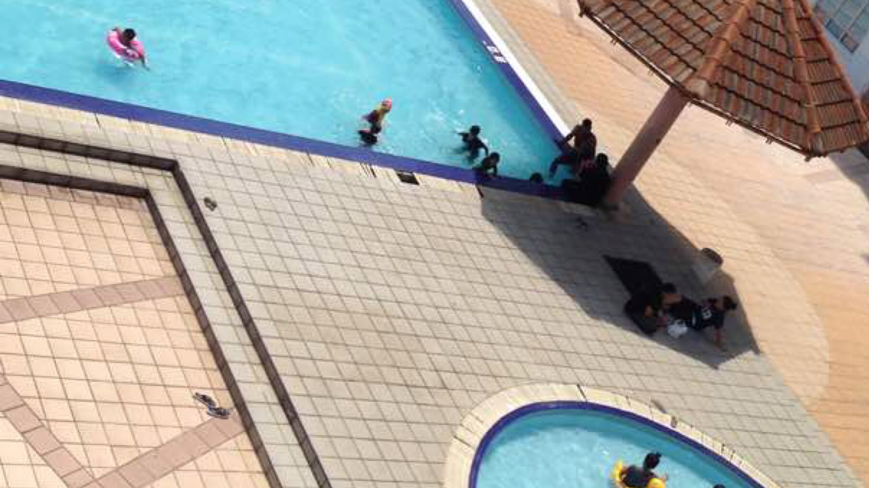 A swimming pool area with tiled flooring, a small pool, and a covered seating area.