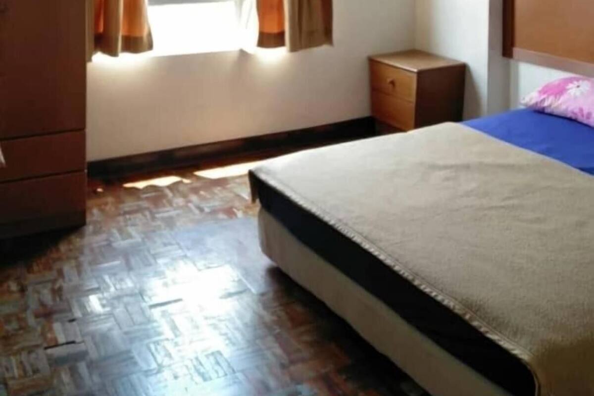 A bedroom with a bed, a wardrobe, a nightstand, and a window with curtains.