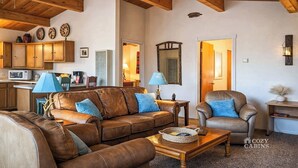 A cozy living room with leather sofas, a coffee table, and wooden beams on the ceiling. There are cabinets and a lamp in the background. - Mama Bears Cabin (Ruidoso)