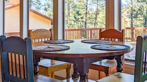 A round wooden table with four chairs, each with a woven placemat. The table is set on a balcony with a wooden railing, and there are trees visible in the background. - Mama Bears Cabin (Ruidoso)