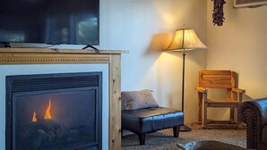 A living room with a fireplace, a television mounted above it, a floor lamp, a leather sofa, and a wooden chair. - Mama Bears Cabin (Ruidoso)