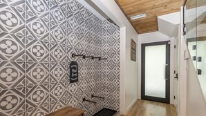 Ein Flur mit Wandfliesen mit Muster, einer Holzbank, einer Metallbank, einer Tür mit Milchglasfenster und einem kleinen Teppich auf dem Boden.