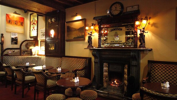 Accogliente interno di un pub con arredi in legno, un camino e un'area bar che espone Guinness e Jameson.