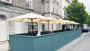 Filea di posti a sedere all'aperto con ombrelloni, una struttura color acquamarina e un edificio con un cartello che riporta la scritta "The Loft".