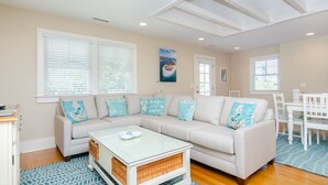 A living room with a beige sofa, white coffee table, and a dining area with a white table and chairs. - Gorgeous Home 1 Block from Ocean and Banks Channel (Wrightsville Beach)