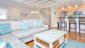 A modern living room with a sofa, coffee table, and kitchen area with bar stools. - Gorgeous Home 1 Block from Ocean and Banks Channel (Wrightsville Beach)