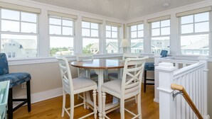 A bright room with a round table and white chairs, large windows, and a ceiling fan. - Gorgeous Home 1 Block from Ocean and Banks Channel (Wrightsville Beach)