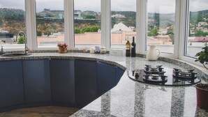 Eine Küche mit einer gebogenen Kücheninsel, Granit-Arbeitsplatten und einem Gasherd. Große Fenster bieten Blick auf eine hügelige Landschaft.