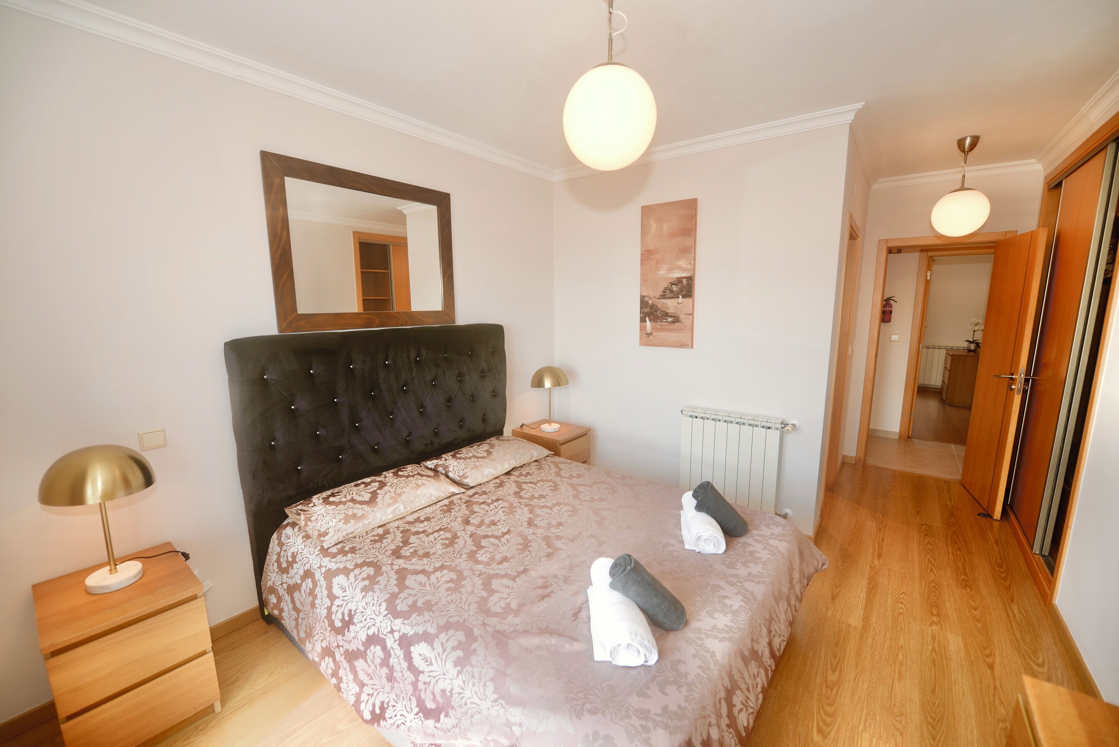 Une chambre à coucher avec un grand lit, une table de chevet, une lampe, un miroir et une porte donnant sur une autre pièce.