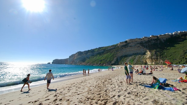Una playa con gente caminando y sentada, acantilados al fondo y el océano.