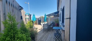 Une terrasse en bois avec des sièges d’extérieur, une petite table et une plante en pot.