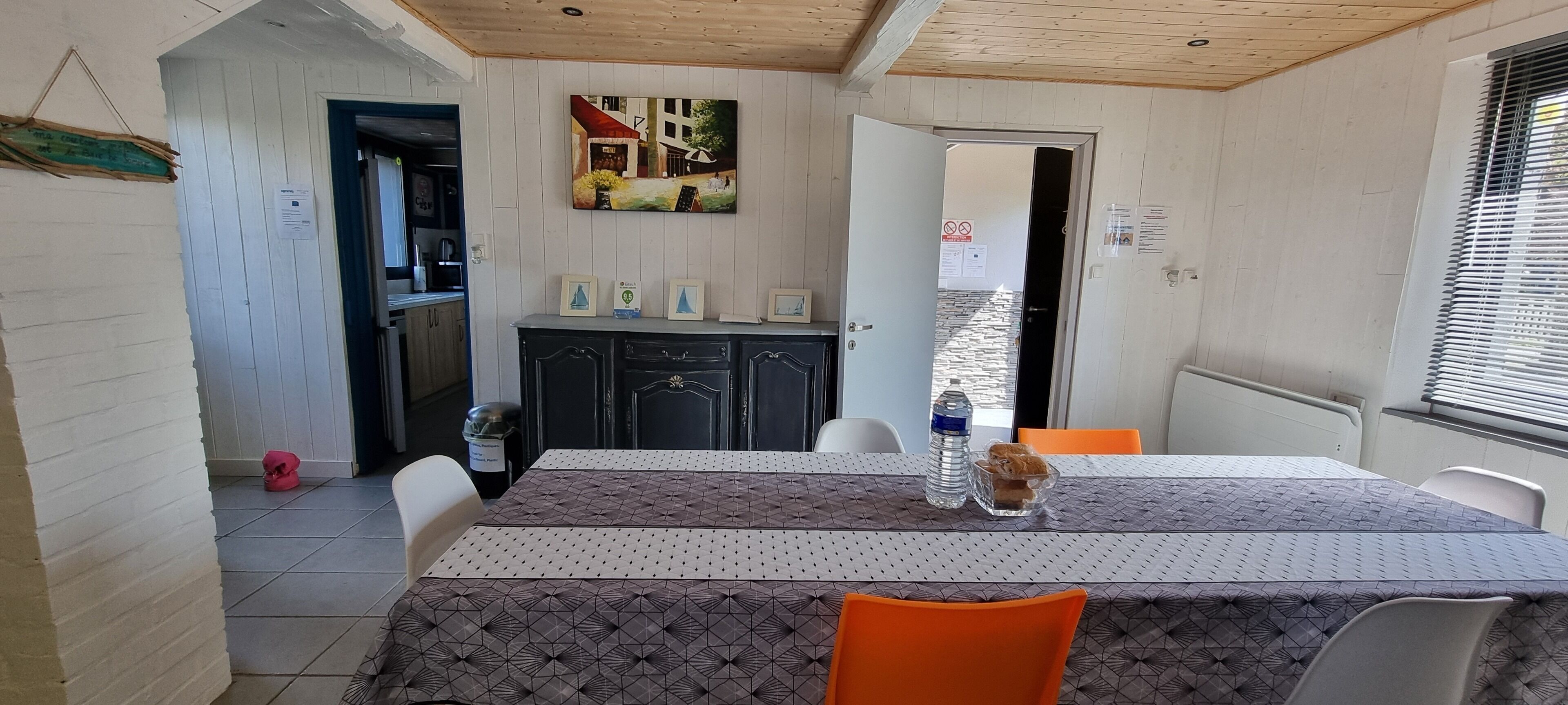 A dining area with a table set for two, a cabinet with framed pictures, and a view of the outside through a door.
