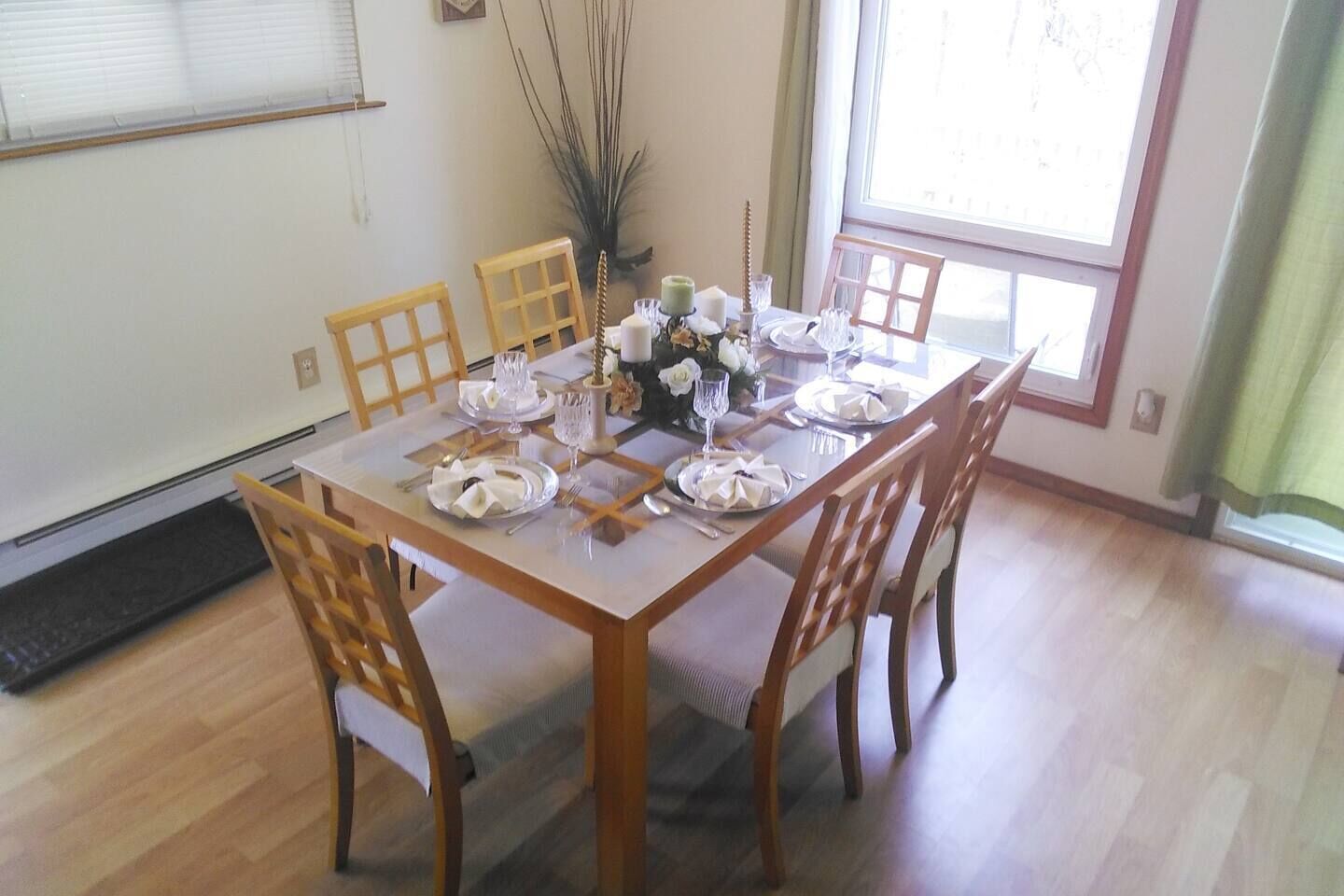 A dining room with a rectangular table set for six, surrounded by wooden chairs.