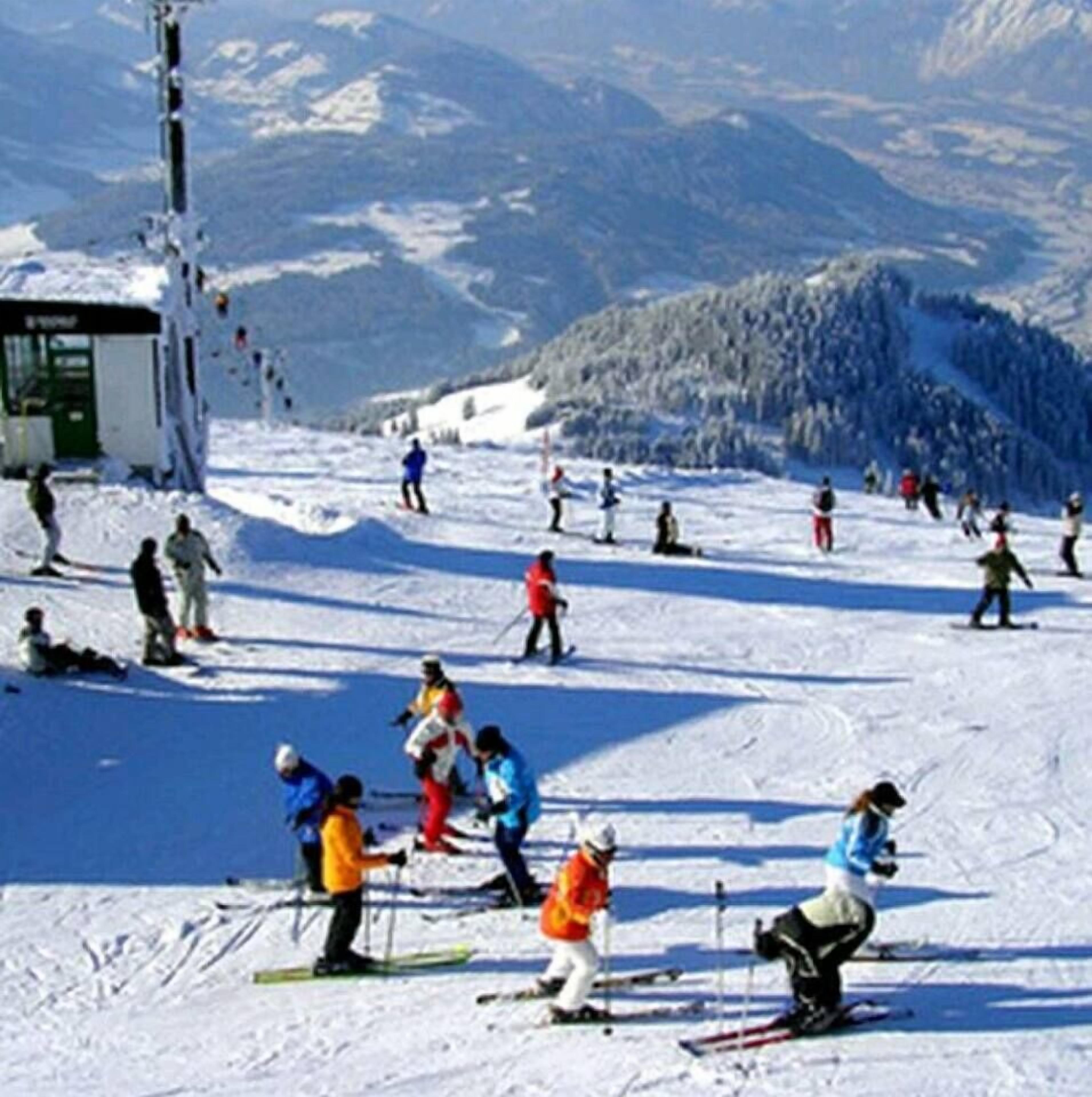 A ski slope with skiers and a small building, likely a lodge, in the background.