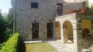 Un bâtiment en pierre doté d’un balcon et d’un espace extérieur aménagé avec des sièges, protégé par un auvent.
