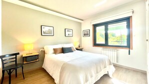 Un dormitorio con una cama, dos mesitas de noche, una silla y una ventana con vistas a la vegetación.