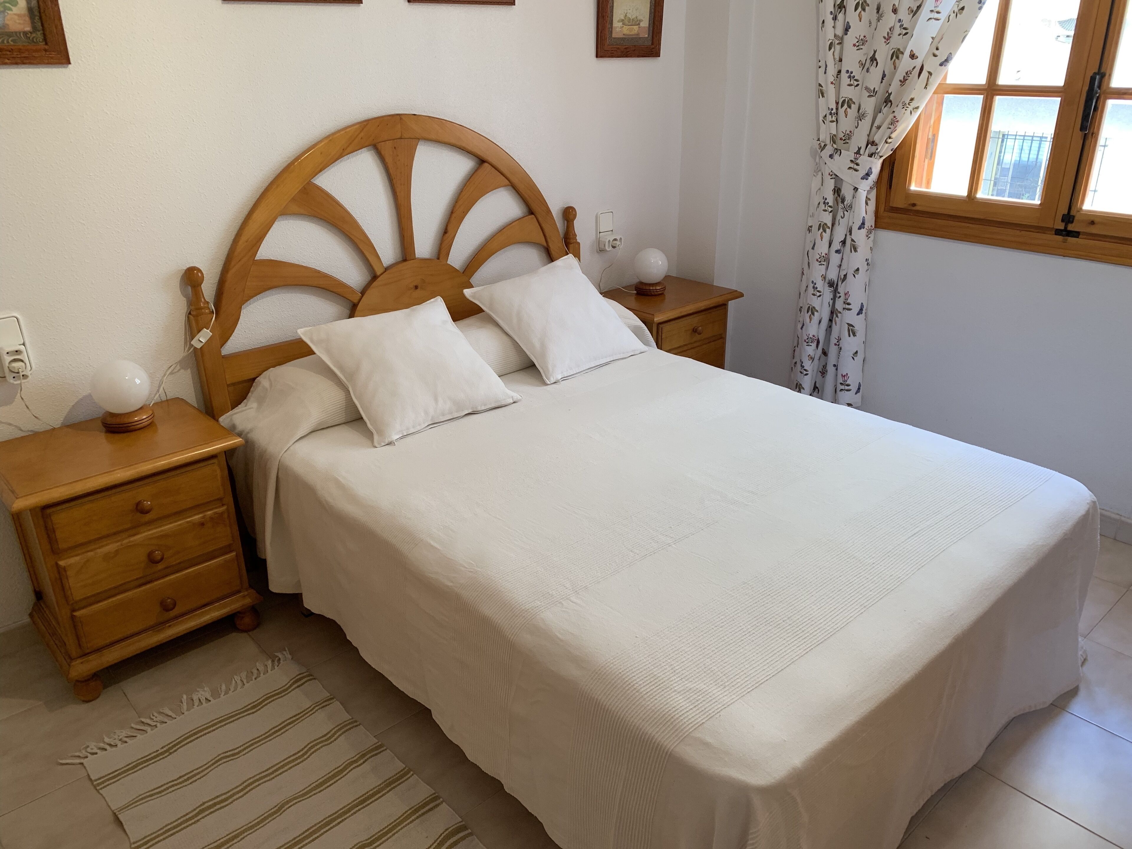 A neatly made bed with a wooden headboard, a bedside table with a lamp, and a nightstand with a drawer.