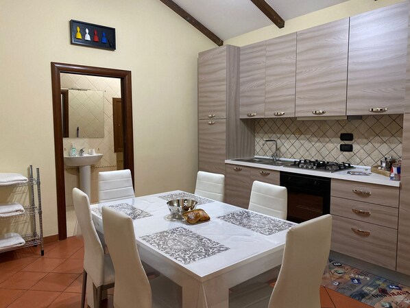A dining area with a table set for four, a kitchen with wooden cabinets, and a tiled backsplash. - Home in Love: VICOLETTO DEI CRIB: APARTMENT WITH TWO BEDROOMS. (NA) (Napoli)