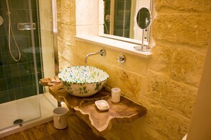 A bathroom with a stone wall, a wooden vanity, a glass shower enclosure, and a bowl sink. - Muragie del Castello (Trani)