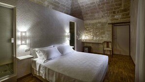 Un dormitorio con techo de piedra, una cama con ropa de cama blanca y una mesita de noche con una lámpara.