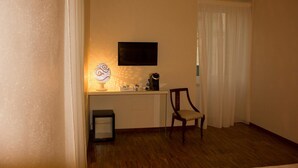 Una habitación pequeña con piso de madera, un escritorio con lámpara, una silla, un televisor y una ventana con cortinas.