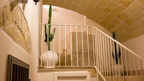 Una escalera con barandilla blanca, pared blanca y una planta de cactus en maceta blanca.