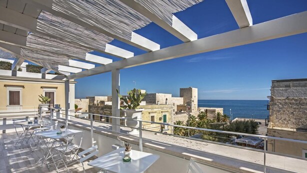 Una terraza con mesas y sillas, con vistas a un pueblo costero y al mar.