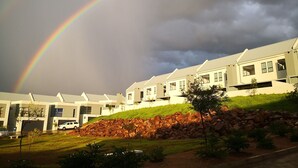 A row of modern houses with a grassy hill and a rainbow in the sky.