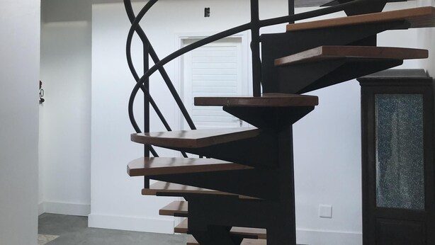 Eine Wendeltreppe mit Holzbodenstufen und Metallgeländern, die zu einer erhöhten Galerie führt.