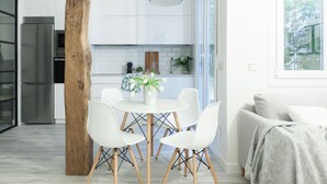 Une cuisine moderne avec des meubles blancs, un îlot central doté de chaises, un réfrigérateur en acier inoxydable et une grande fenêtre donnant sur un paysage verdoyant.