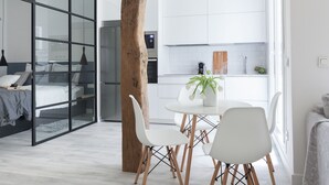 Une pièce moderne et bien éclairée, comprenant un lit, une table à manger avec des chaises, un coin cuisine et une grande fenêtre.