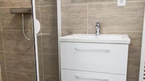 Un bagno moderno con box doccia in vetro, un mobile lavabo bianco con specchio e pavimento piastrellato.