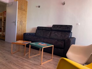 A living room with a dark sofa, two small wooden tables, a yellow chair, and a white wardrobe. - Large apartment 43 m2 -6 people - 4 stars GOLD - Ideally located (val thorens)