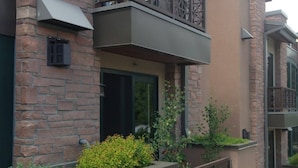 Ein zweistöckiges Gebäude mit Ziegelaußenwand, einem Balkon mit Gittergeländer und einem kleinen Garten mit verschiedenen Pflanzen und Blumen.